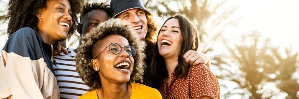 Group photo of diverse adults in front of trees while all laughing